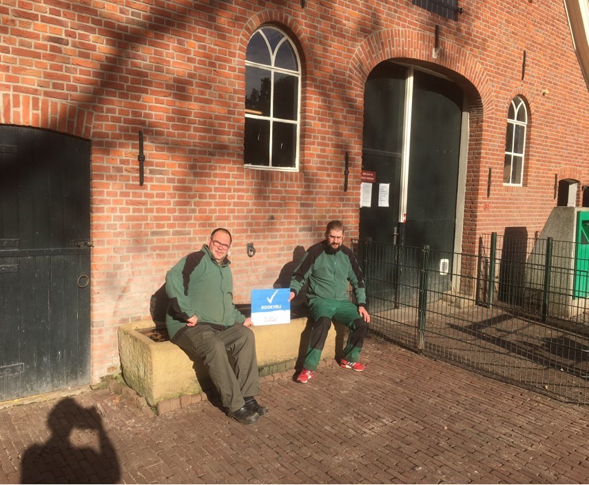 Twee medewerkers van kinderboerderij Erve ’t Wooldrik in Enschede met tussen hen in een bordje met tekst 'Rookvrij'
