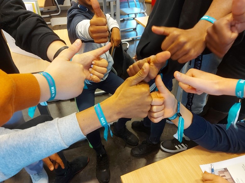 Leerlingen dragen blauwe armbandjes met daarop de tekst 'Ik ben Smokefree' en steken hun duim omhoog.