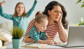 gestresste moeder achter laptop met kind op schoot en druk kind op de achtergrond